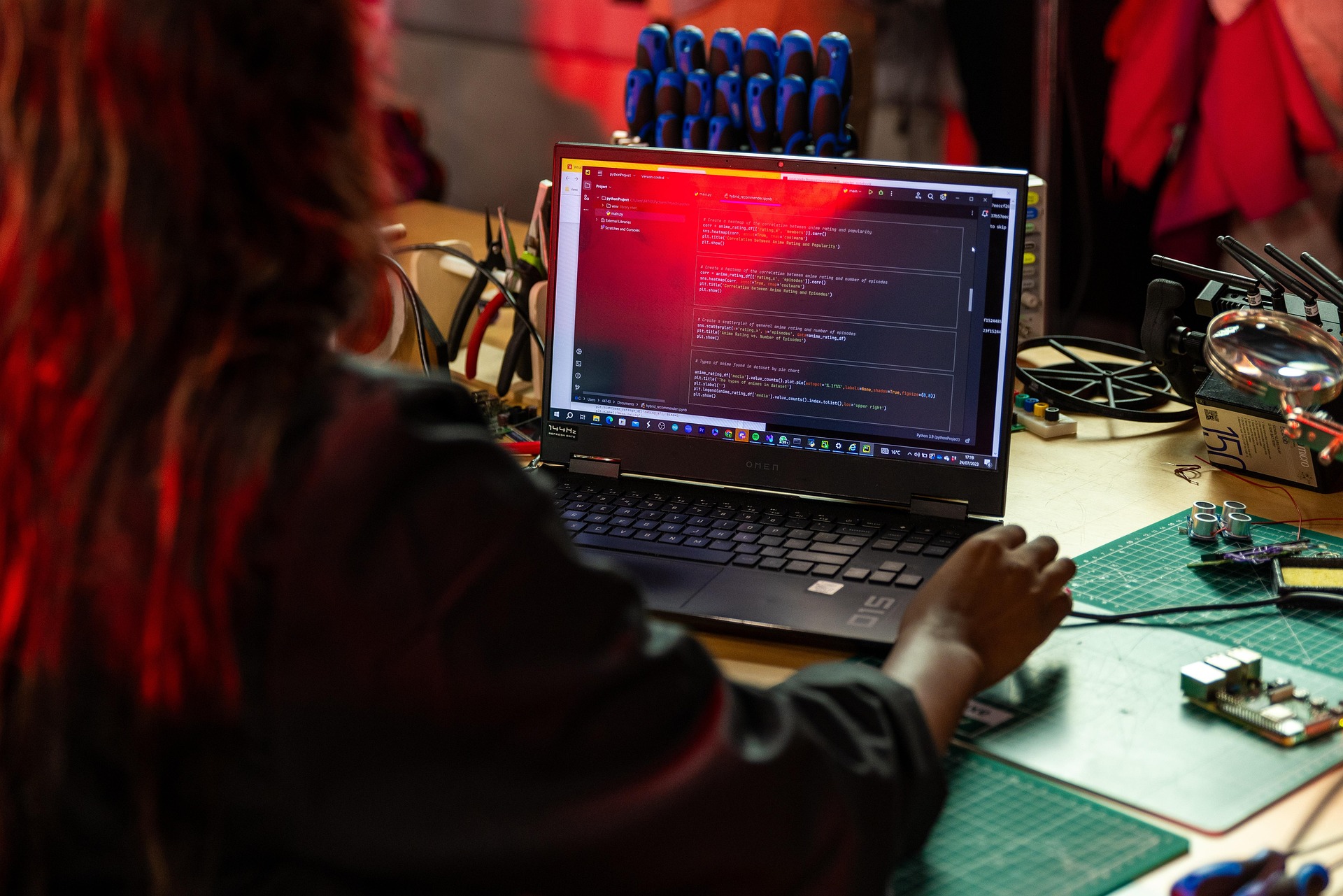 Person arbeitet an einem Laptop an einem technischen Arbeitsplatz mit Werkzeugen und Elektronik