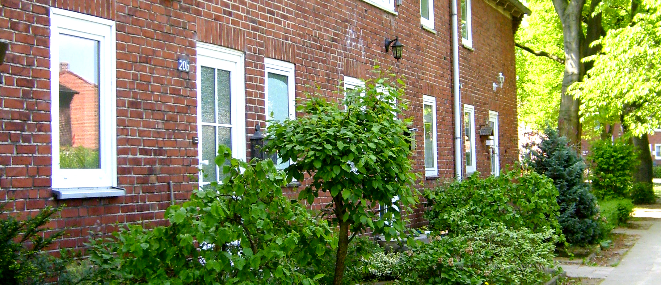 Backstein-Wohngebäude mit weißen Fenstern und begrüntem Vorgarten